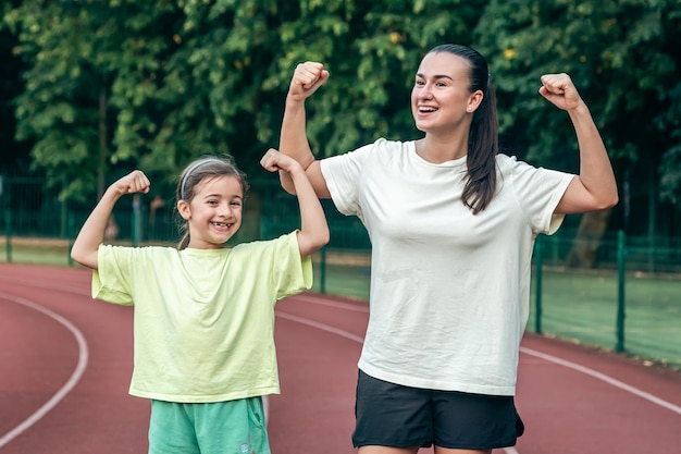 Foto gratuita una mujer y su hija muestran sus bíceps entrenando en el estadio.