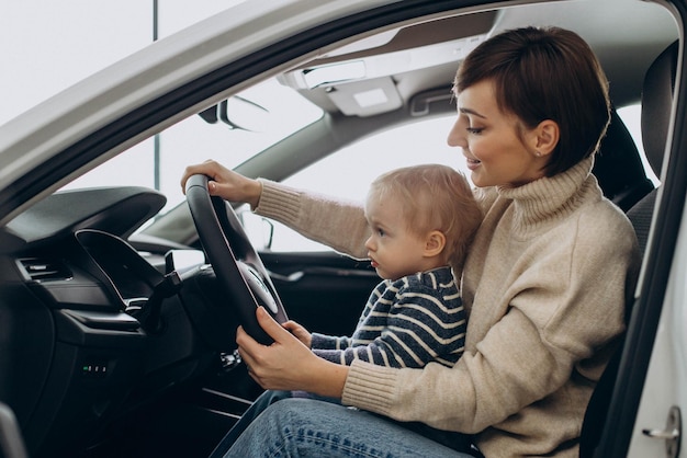 Mujer con su hijo pequeño sosteniendo el volante en un automóvil en una sala de exposición de automóviles