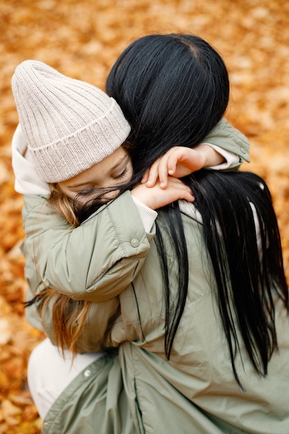 Mujer y su niña jugando en el bosque de otoño y riendo Hombre morena abrazando a su hija Familia vistiendo abrigos verdes