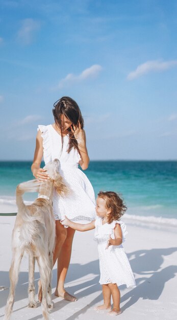 Mujer con su pequeña hija jugando con perros en la playa junto al mar