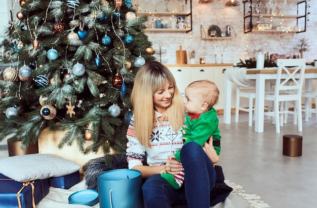 Mujer con su pequeño hijo sentarse en el árbol de Navidad