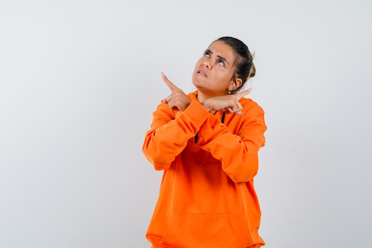 Foto gratuito mujer en sudadera con capucha naranja apuntando hacia otro lado y mirando vacilante