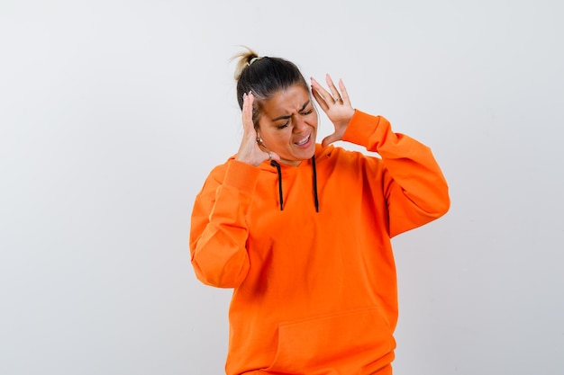 Mujer en sudadera con capucha naranja levantando las manos de manera agresiva