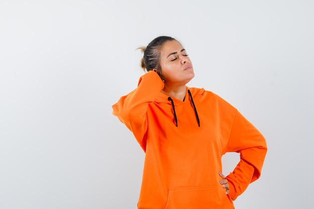 Mujer en sudadera con capucha naranja manteniendo la mano detrás de la cabeza y mirando relajado