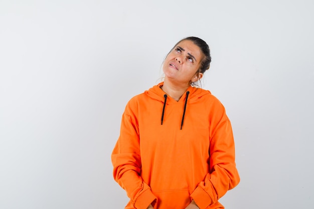 Foto gratuita mujer en sudadera con capucha naranja mirando hacia arriba y mirando vacilante