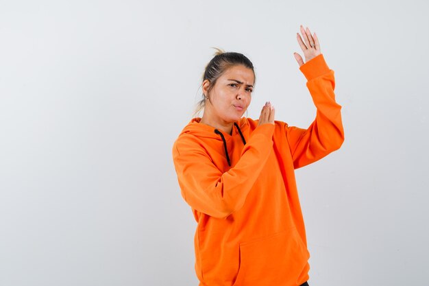 Mujer en sudadera con capucha naranja mostrando gesto de tajo de karate y mirando rencoroso