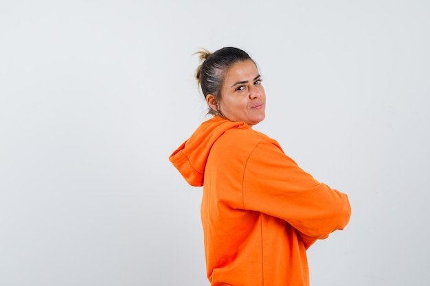 Mujer en sudadera con capucha naranja de pie con los brazos cruzados y mirando confiado