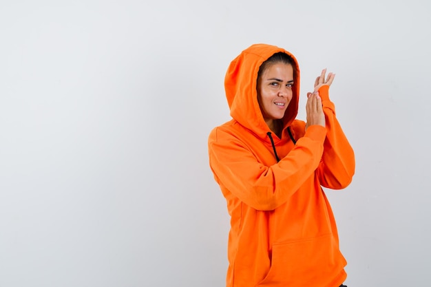 Mujer en sudadera con capucha naranja posando mientras está de pie y mirando seductor
