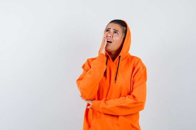 Mujer en sudadera con capucha naranja sosteniendo la mano cerca de la boca y mirando preocupado
