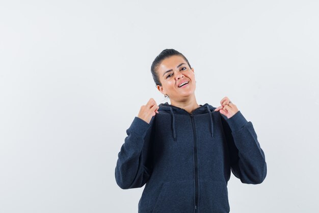 Mujer con sudadera con capucha tirando de su cuello y mirando orgullosa, vista frontal.