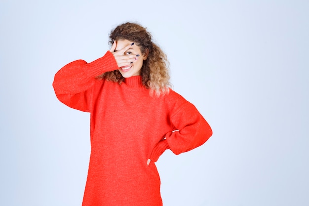 mujer en sudadera roja mirando a través de sus dedos.