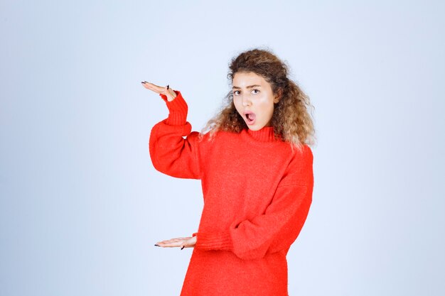 mujer en sudadera roja mostrando las medidas de un objeto.