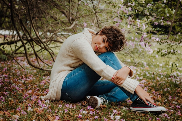 Mujer en suéter beige y jeans azul sentado en el bosque