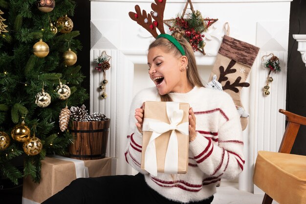 Mujer en suéter blanco mostrando felizmente presente en el diseño de interiores de Navidad.