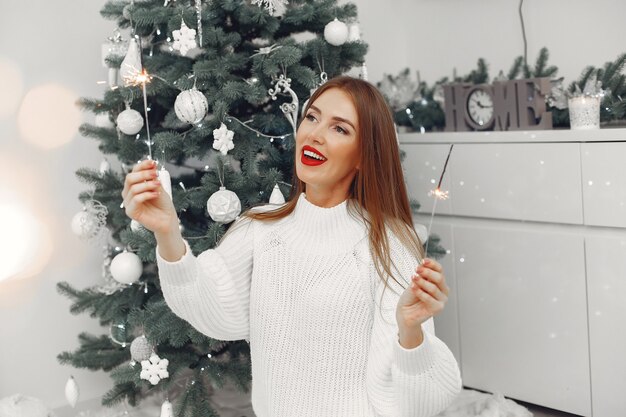 Mujer con un suéter blanco sentada junto al árbol de navidad