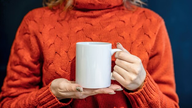 Mujer en suéter naranja sosteniendo una taza blanca con ambas manos,