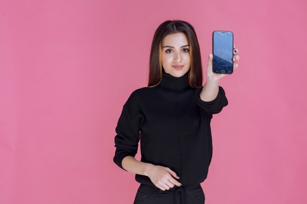 Mujer de suéter negro sosteniendo un teléfono inteligente.