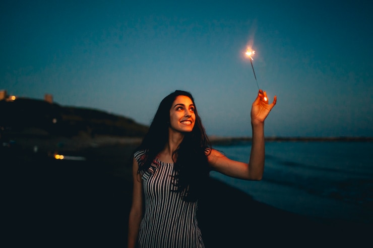 Foto gratuito mujer sujetando bengala en una playa de noche