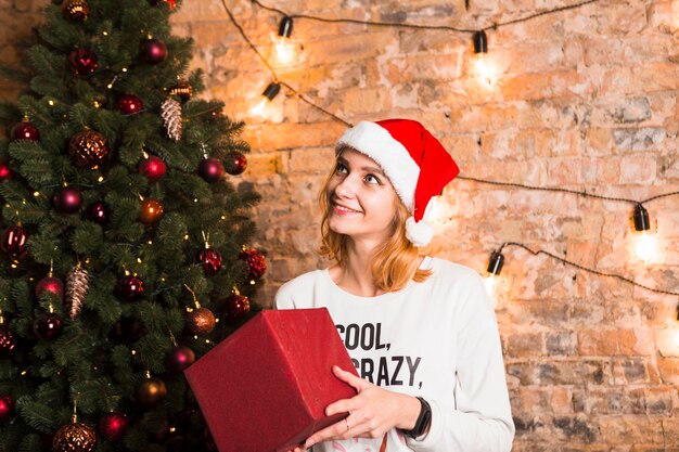 Mujer sujetando caja de regalo al lado de árbol de navidad