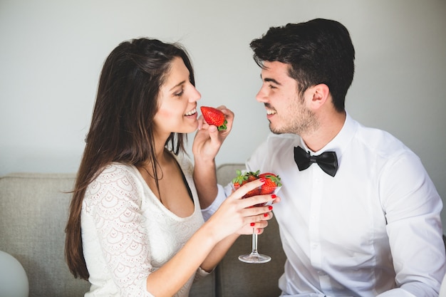Mujer sujetando una copa con fresas y el hombre dando de comer a ella una