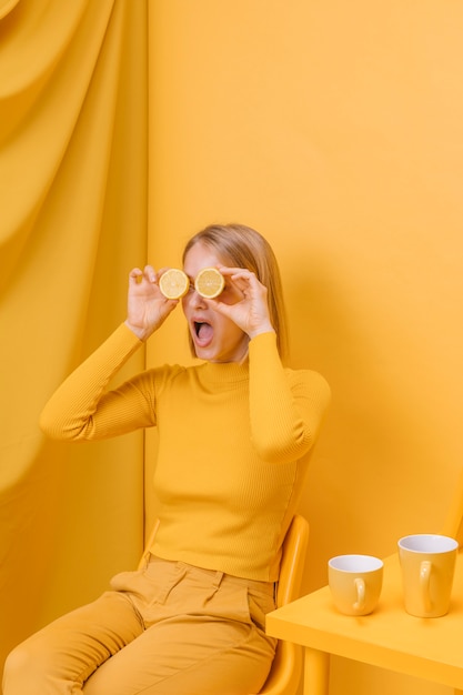 Mujer sujetando limones enfrente de sus ojos en un escenario amarillo