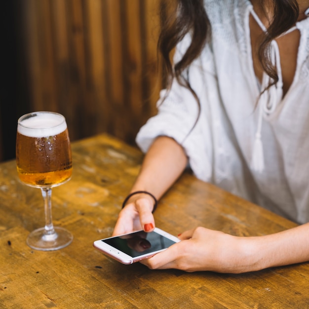 Mujer sujetando smartphone al lado de cerveza