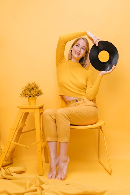 Mujer sujetando un vinilo en un escenario amarillo