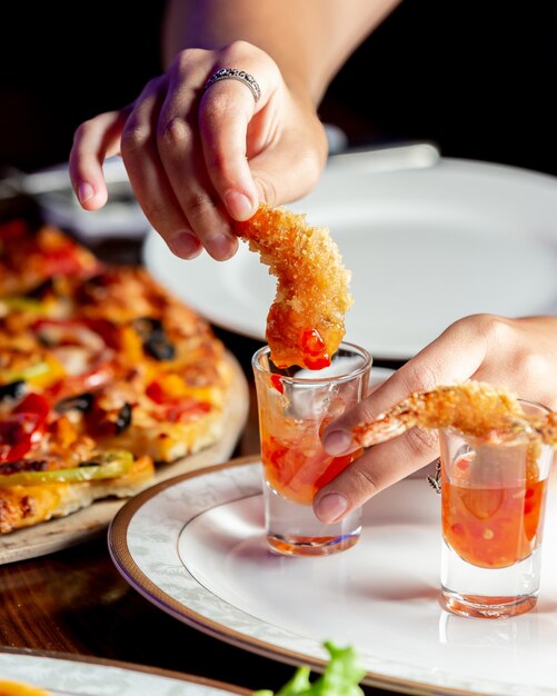 Mujer sumergiendo crujientes gambas fritas en salsa de chile dulce en vaso de chupito