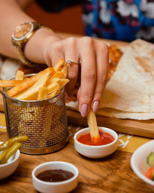 Mujer sumergiendo papas fritas en salsa de tomate en el restaurante.