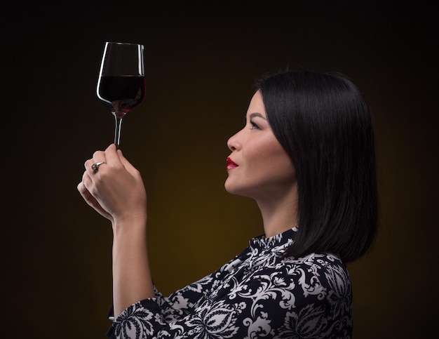 Foto gratuita mujer sumiller asiática mirando una copa de vino tinto con mucha atención.