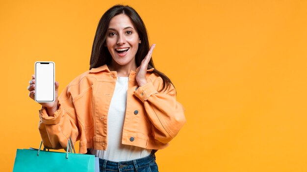 Mujer super emocionada sosteniendo smartphone y bolsas de compras
