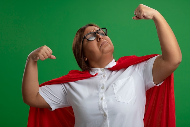 Foto gratuita mujer de superhéroe de mediana edad confiada con gafas que muestra un gesto fuerte aislado sobre fondo verde