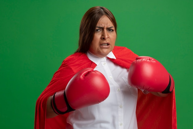 Mujer de superhéroe de mediana edad confiada con guantes de boxeo de pie en pose de lucha aislada en verde