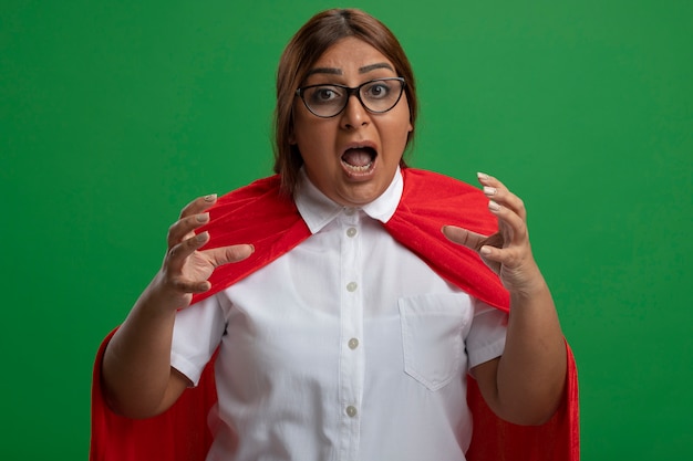 Mujer de superhéroe de mediana edad enojada con gafas cogidos de la mano alrededor de la cara aislada en verde