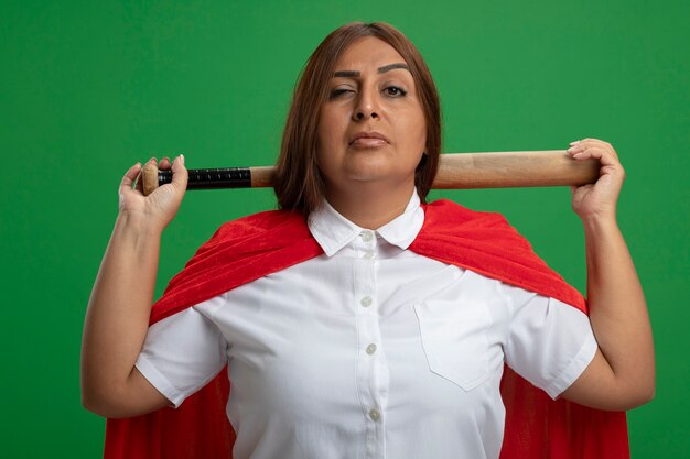 Foto gratuita mujer de superhéroe de mediana edad segura que sostiene un bate de béisbol detrás del cuello aislado en verde