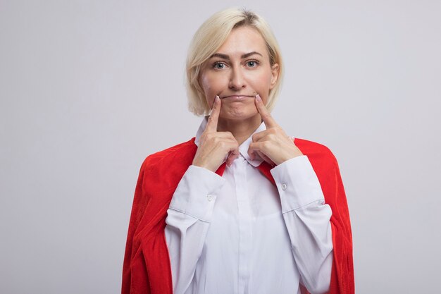 Mujer de superhéroe rubia de mediana edad en capa roja haciendo sonrisa falsa