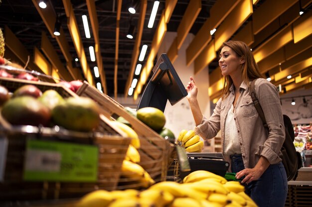 Mujer en el supermercado con balanza digital de autoservicio para medir el peso de la fruta