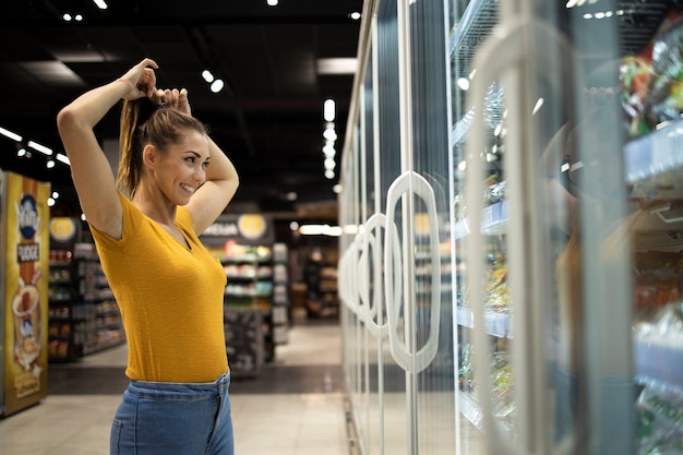 Mujer en el supermercado eligiendo alimentos en el congelador