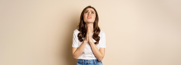 Mujer suplicando mendicidad y buscando ayuda desesperada de pie sobre fondo beige