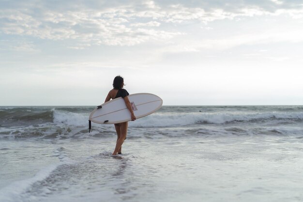 Mujer surfista con tabla de surf en el océano al atardecer