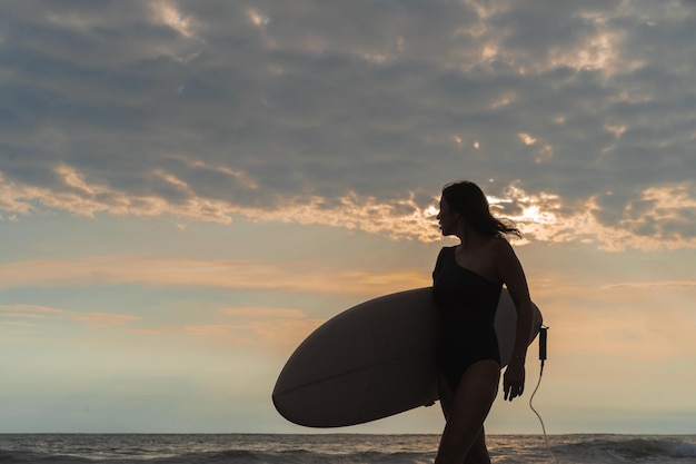 Mujer surfista con tabla de surf en el océano al atardecer