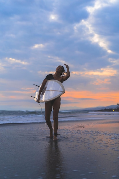 Mujer surfista con tabla de surf en el océano al atardecer.