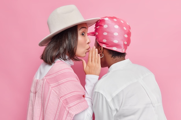 Foto gratuita mujer susurra chismes en amigos oreja weas sombrero y camisa aislado en rosa