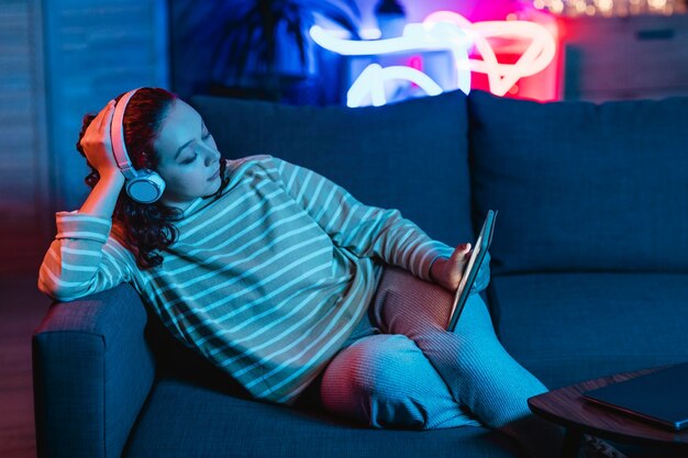 Mujer con tableta y auriculares en casa en el sofá