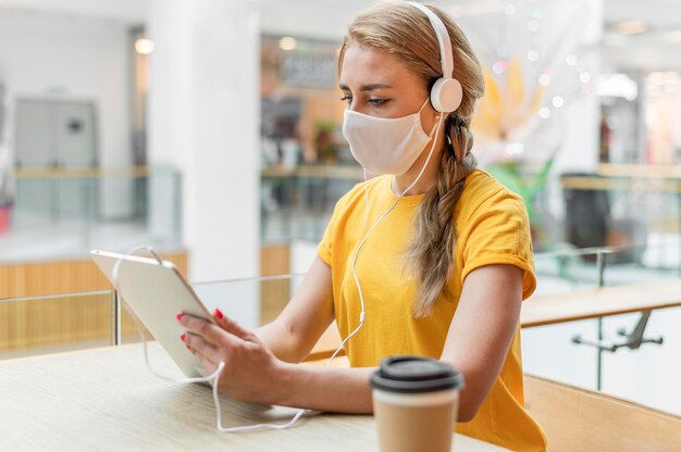 Mujer con tableta y auriculares con máscara