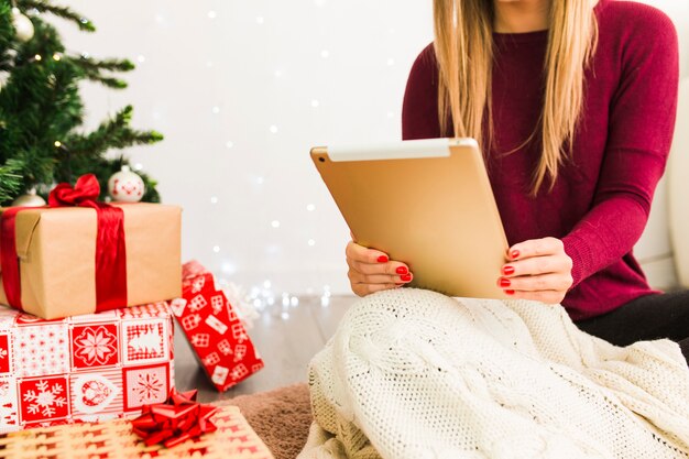 Mujer con tableta cerca de cajas de regalo y árbol de navidad