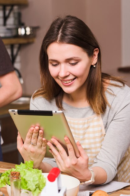 Mujer en tableta de la navegación del delantal en cocina