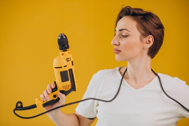 Mujer con taladro eléctrico sobre fondo amarillo