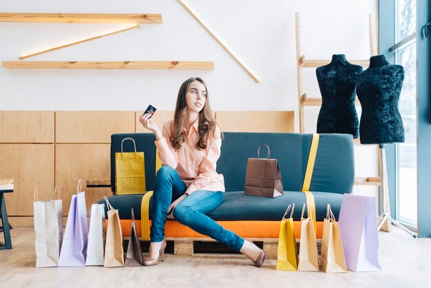 Mujer con tarjeta de crédito y bolsas de papel en el sofá