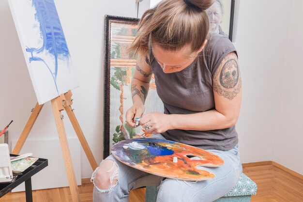 Mujer tatuada mezclando pinturas en la paleta
